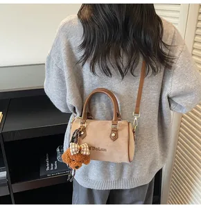 Detail of khaki suede Boston bag with leather handles and a cute teddy bear charm