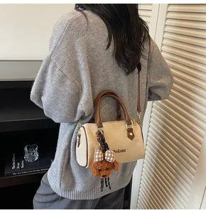 Detail view of beige suede Boston bag with brown handles and teddy bear charm on model