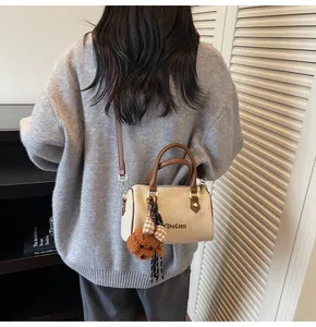 Detail of beige Boston bag with brown handles and a cute teddy bear plush pendant