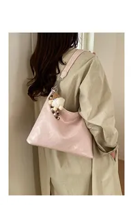 Sac bandoulière en cuir verni plissé rose avec breloque porté par un mannequin femme