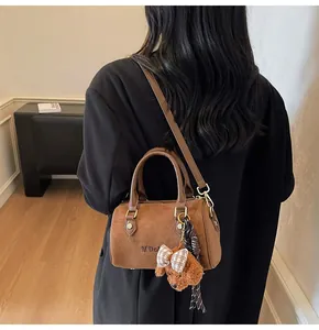 Detail of dark brown suede boston bag with golden hardware and plush dog charm