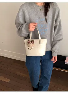 Detail van een beige emmertas met een pluche beer hanger en een stippen strikje