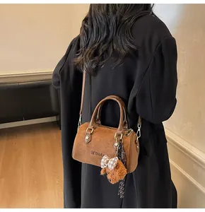 Close-up of brown suede Boston bag with MDolin logo and teddy bear charm accessory