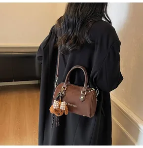 Detail of dark brown suede mini Boston bag with plush dog charm worn by a model