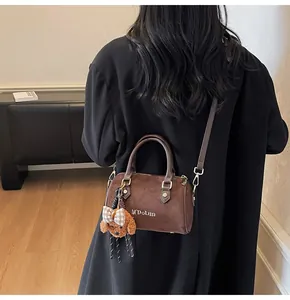 Detail of vintage brown suede barrel bag with teddy bear charm on black coat