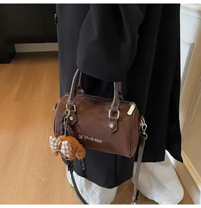 Detail of dark brown suede Boston bag with M'DOLUN text and cute bear charm accessory