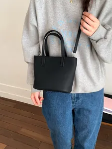 Minimalistische zwarte bucket bag van generfd leer met handvaten en schouderriem