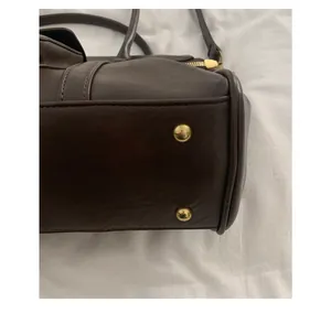 Détail d'un sac en cuir marron foncé avec pieds en métal doré et coutures de précision
