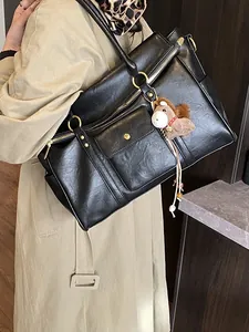 Grand sac cabas en cuir noir avec détails dorés et breloque porté par un mannequin