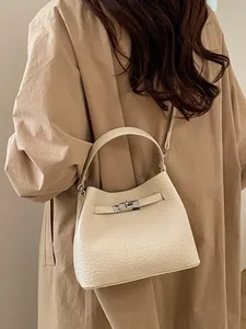 Beige textured leather bucket bag with silver clasp, worn with a stylish khaki trench coat