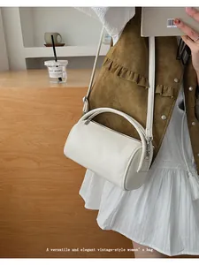 Beige zylindrische Baguette-Tasche mit Tragegriff und Schultergurt getragen von Model