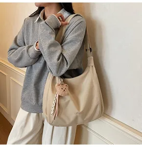 Detail of light khaki canvas tote bag with wide strap and brown bear plush charm
