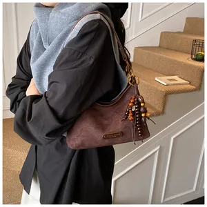 Detail of dark brown suede crescent bag with beaded tassel and metal logo plaque