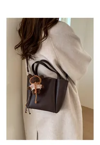Détail d'un sac seau en cuir grainé marron foncé avec un charmant petit ours en tricot