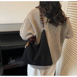 Detail of black suede tote bag featuring a retro wooden beaded shoulder strap and sleek design
