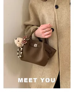 Close-up of brown lychee grain leather bucket bag with plush dog charm and silver lock detail