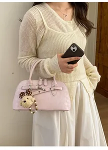 Detail of light pink faux leather handbag with a plush bear charm on a beige knit cardigan