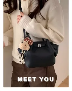 Detail of black pebbled leather bucket bag with silver buckle and plush bear charm