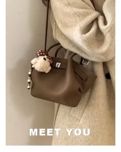 Detail view of brown leather bucket bag with plush dog charm on a white coat model