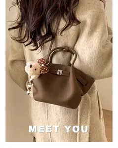 Detail view of brown pebbled leather bucket bag with metal clasp and plush bear charm