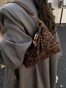 Leopard print crossbody bag with wooden bead tassels and leather strap on a grey coat