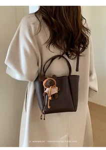 Détail d'un sac seau en cuir grainé marron foncé avec un charmant ours en peluche