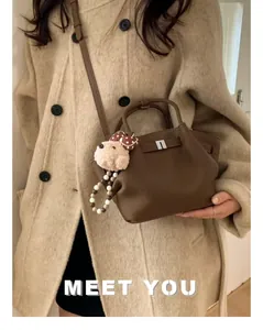 Close-up of brown litchi pattern leather bucket bag with cute plush puppy charm pendant