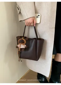 Détail d'un sac seau marron foncé avec un pendentif ours en peluche sur un manteau