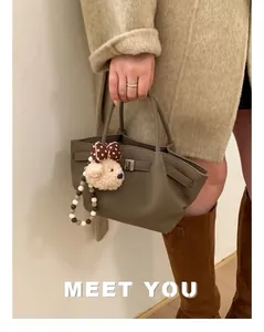 Detail of grey leather bucket bag with metal buckle and cute plush bear charm accessory
