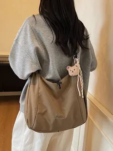 Brown canvas crossbody tote bag with adjustable strap and cute plush bear charm decoration