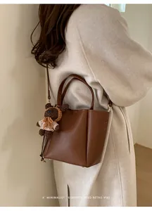 Détail d'un sac seau en cuir marron foncé avec un charm ours sur un manteau beige