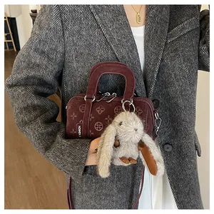Detail of dark red embossed baguette bag with a plush bunny charm and fashion tag