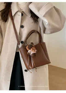 Détail du sac seau rétro en cuir marron avec charme d'ours sur un manteau en laine beige