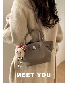 Detail of brown litchi leather bucket bag with cute bear charm and crossbody strap