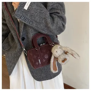 Detail of dark red cylinder bag with floral embossing and plush bunny keychain accessory