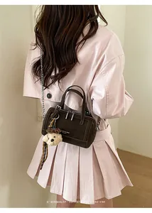 Detail of dark brown mini Boston bag with plush bear charm and chain strap on model