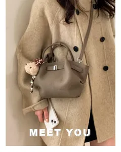 Detail of taupe lychee leather bucket bag with metal clasp and cute plush bear charm
