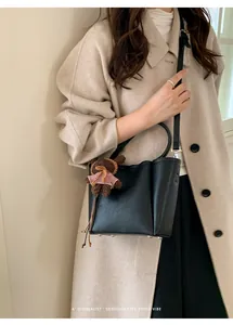 Détail du sac seau noir avec un charm ours en tricot marron et une poignée supérieure