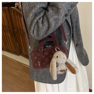 Detail of burgundy crossbody baguette bag with clover embossing and rabbit charm