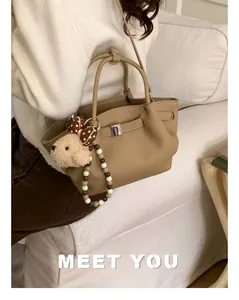 Detail of khaki bucket bag with plush dog charm and elegant pearl beaded handle