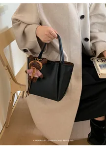 Détail d'un sac seau en cuir grainé noir avec un charmant ours en peluche marron attaché