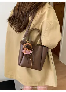 Sac seau marron avec charm ours en peluche porté à l'épaule par un mannequin en studio