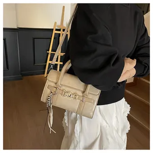 Détail du sac baguette en cuir mat beige avec boucle métallique et pompon sur le mannequin