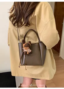 Détail du sac seau en cuir marron foncé avec un charm d'ours et une bandoulière élégante