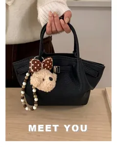Detail of black pebbled leather bucket bag with teddy bear charm and bead chain
