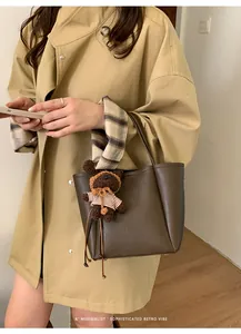 Détail du sac seau en cuir marron foncé avec un porte-clés ours en peluche sur l'anse