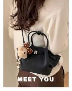 Detail of black leather bucket bag with pebble texture and cute bear charm shown on model
