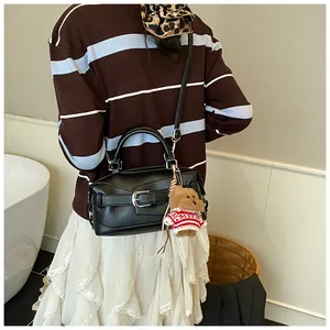 Détail d'un sac baguette noir en cuir avec boucle argentée et charm d'ourson en peluche