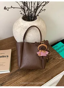 Gros plan d'un sac seau en cuir marron avec un ourson en peluche sur une table en bois