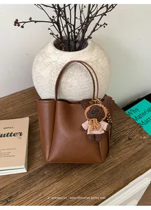 Détail du sac seau en cuir marron foncé avec breloque ours sur une table en bois